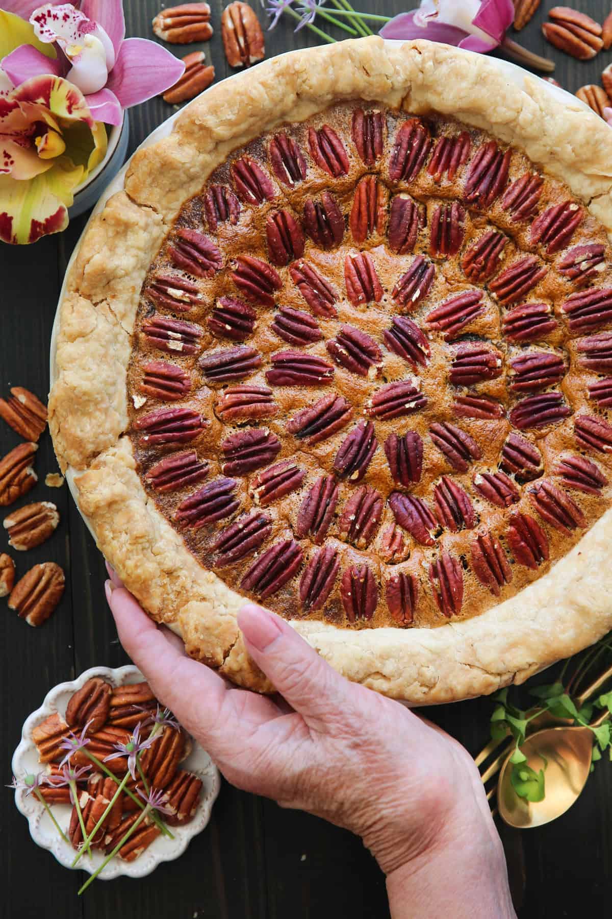 Classic Homemade Pecan Pie Pecan Pie in a white pie dish with one hand holding the side of the pie dish.