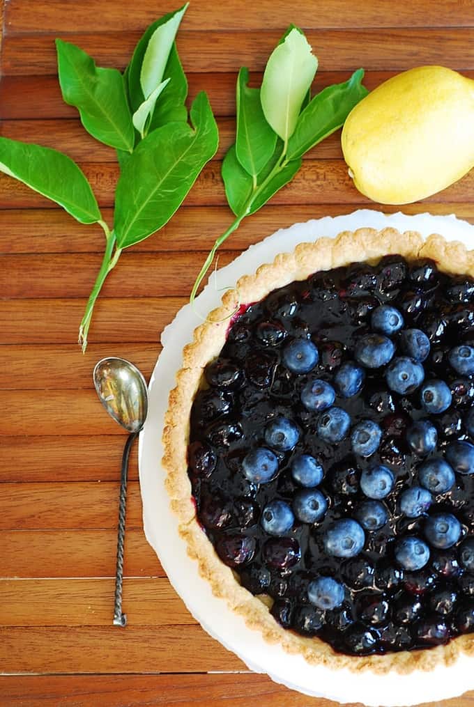 Blueberry Tart on a wooden background with the spoon next to it and a lemon (overhead shot)