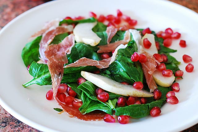 Spinach salad with pomegranate seeds, pears, and prosciutto