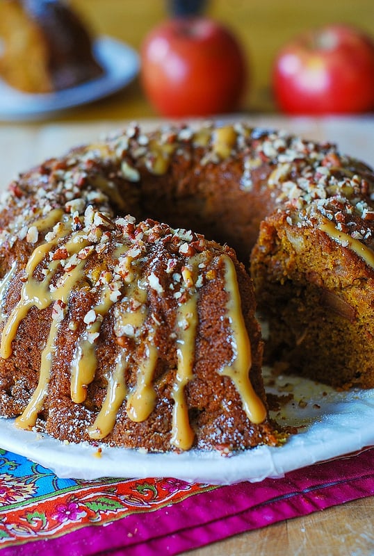 Apple pumpkin cinnamon and vanilla bundt cake with dulce de leche drizzle and pecans on a white plate