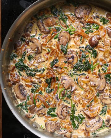 caramelized onion sauce with spinach and mushrooms in a stainless steel pan.