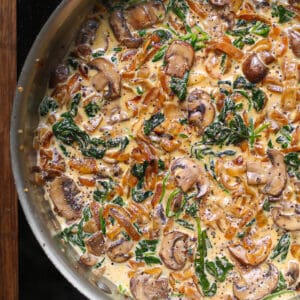 creamy caramelized onion sauce with spinach and mushrooms in a stainless steel pan.