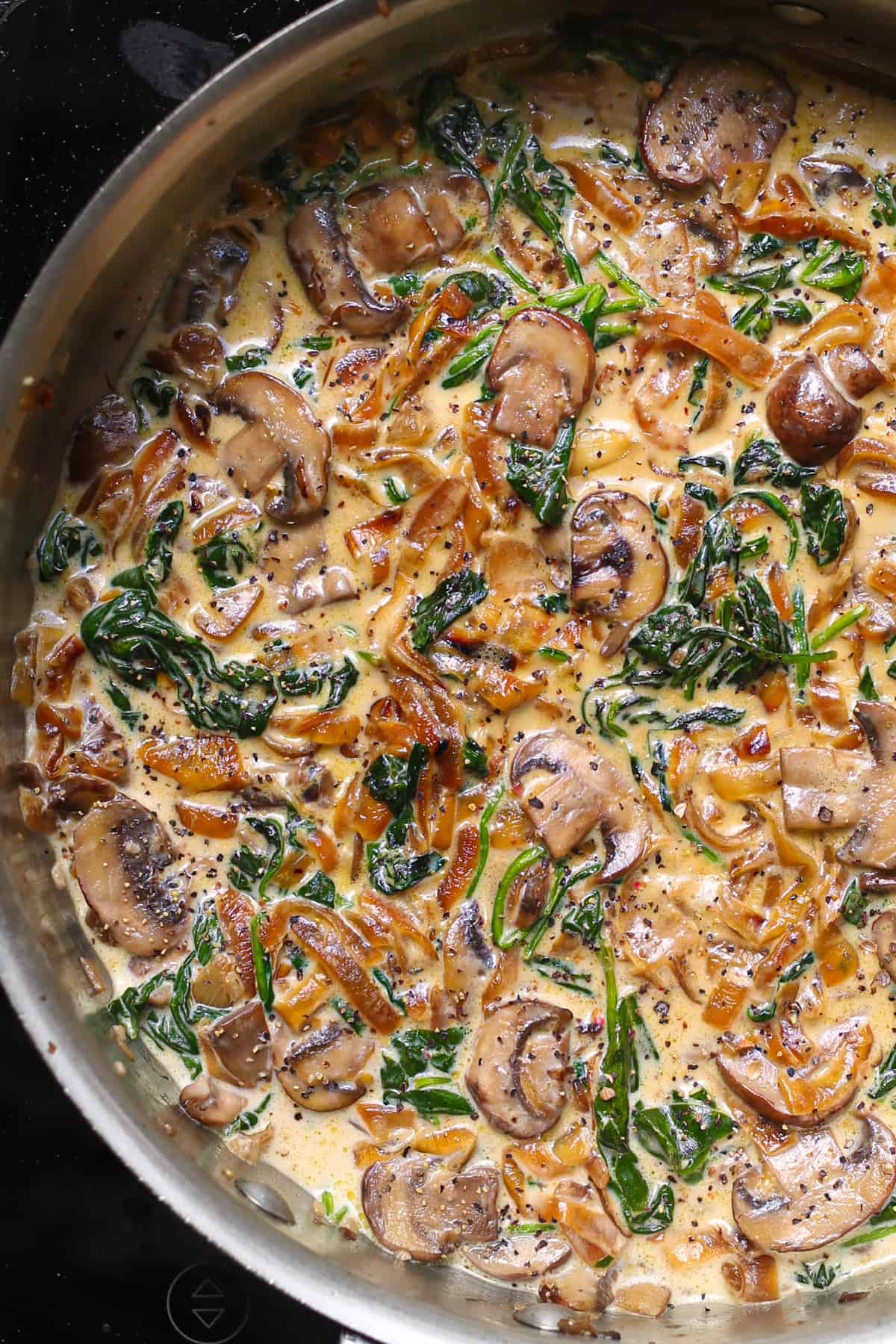 mushroom sauce with caramelized onions and spinach in a stainless steel pan.