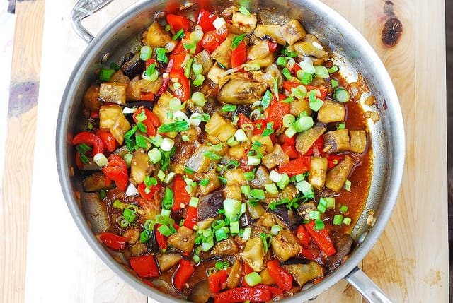 adding chopped green onions to the skillet with eggplant and red bell peppers