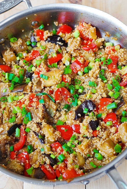 adding quinoa to the skillet with eggplant and bell peppers