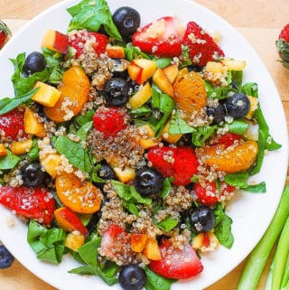 Quinoa salad with spinach, strawberries, blueberries, peaches, mandarin oranges in a homemade Balsamic vinaigrette dressing on a white plate