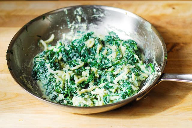 Mixing spinach, garlic, ricotta cheese, and mozzarella cheese for the lasagna in a stainless steel skillet