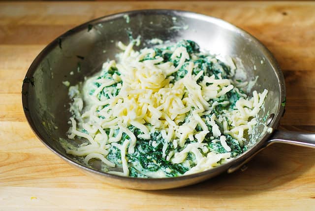 Mixing spinach, ricotta cheese, and mozzarella cheese in a stainless steel skillet