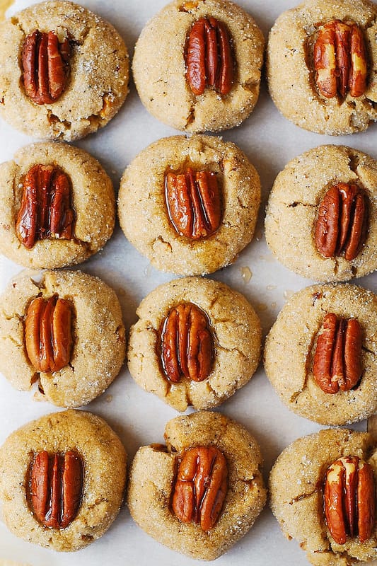 Browned Butter Pecan Cookies with Pecans on top and brushed with maple syrup on parchment paper