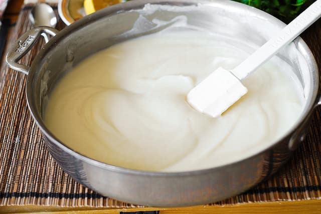 making cauliflower alfredo sauce in a large skillet with a spatula