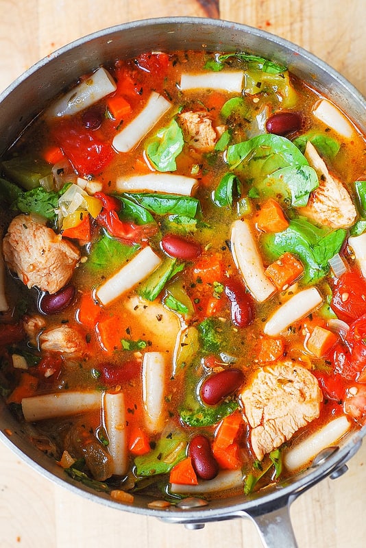 Chicken vegetable pasta soup with bell peppers, carrots, tomatoes, red kidney beans, spinach, garlic