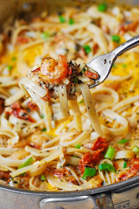 fork lifting pasta and shrimp from the stainless steel skillet filled with spicy shrimp pasta