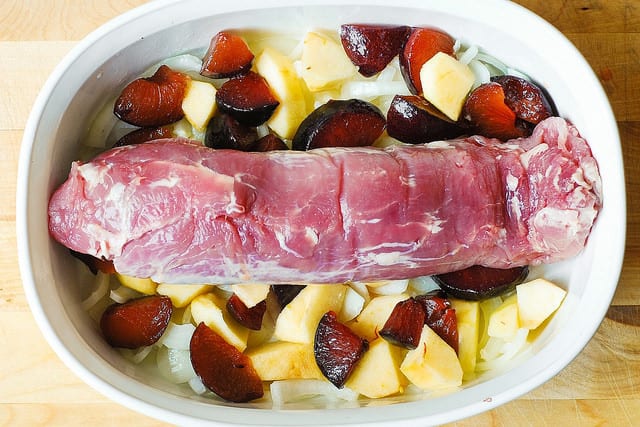 adding pork tenderloin on top of apples, plums, and onions in a casserole dish (process shot)