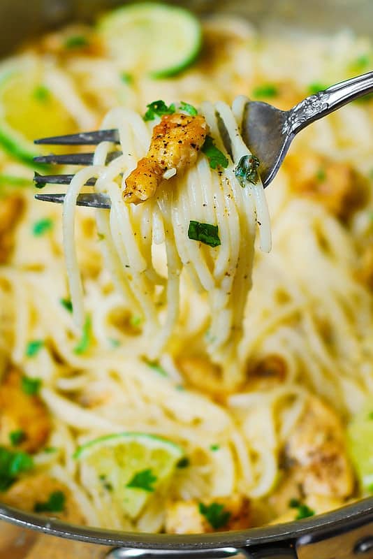 Chicken Pasta with Creamy Cilantro-Lime Sauce lifted on a fork above the stainless steel skillet filled with pasta