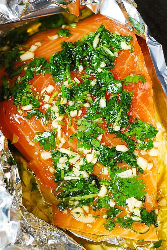 raw salmon fillet with chopped fresh cilantro and chopped garlic in a foil