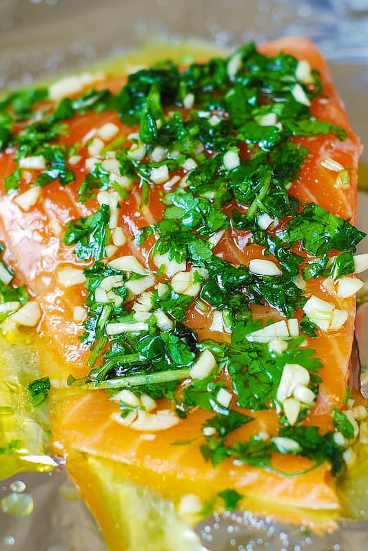 chopped fresh cilantro, chopped garlic on top of raw salmon on a foil