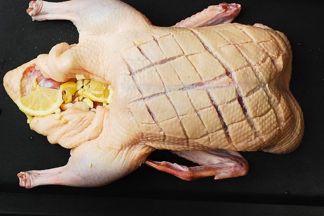 folding the duck's flapping skin on both ends inwards, to hold the minced garlic and lemon slices inside the duck's cavity