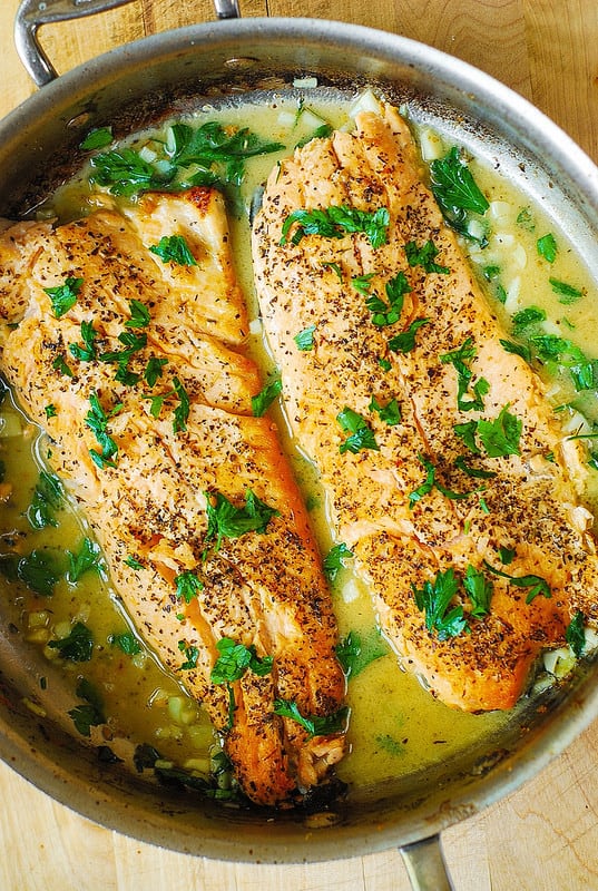 2 Trout fillets seasoned with Italian seasoning, topped with chopped fresh parsley with Garlic Lemon Butter Herb Sauce in a stainless steel skillet