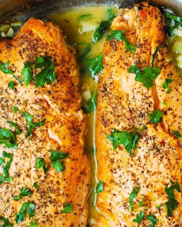 2 trout fillets in a garlic butter lemon sauce in a stainless steel pan.