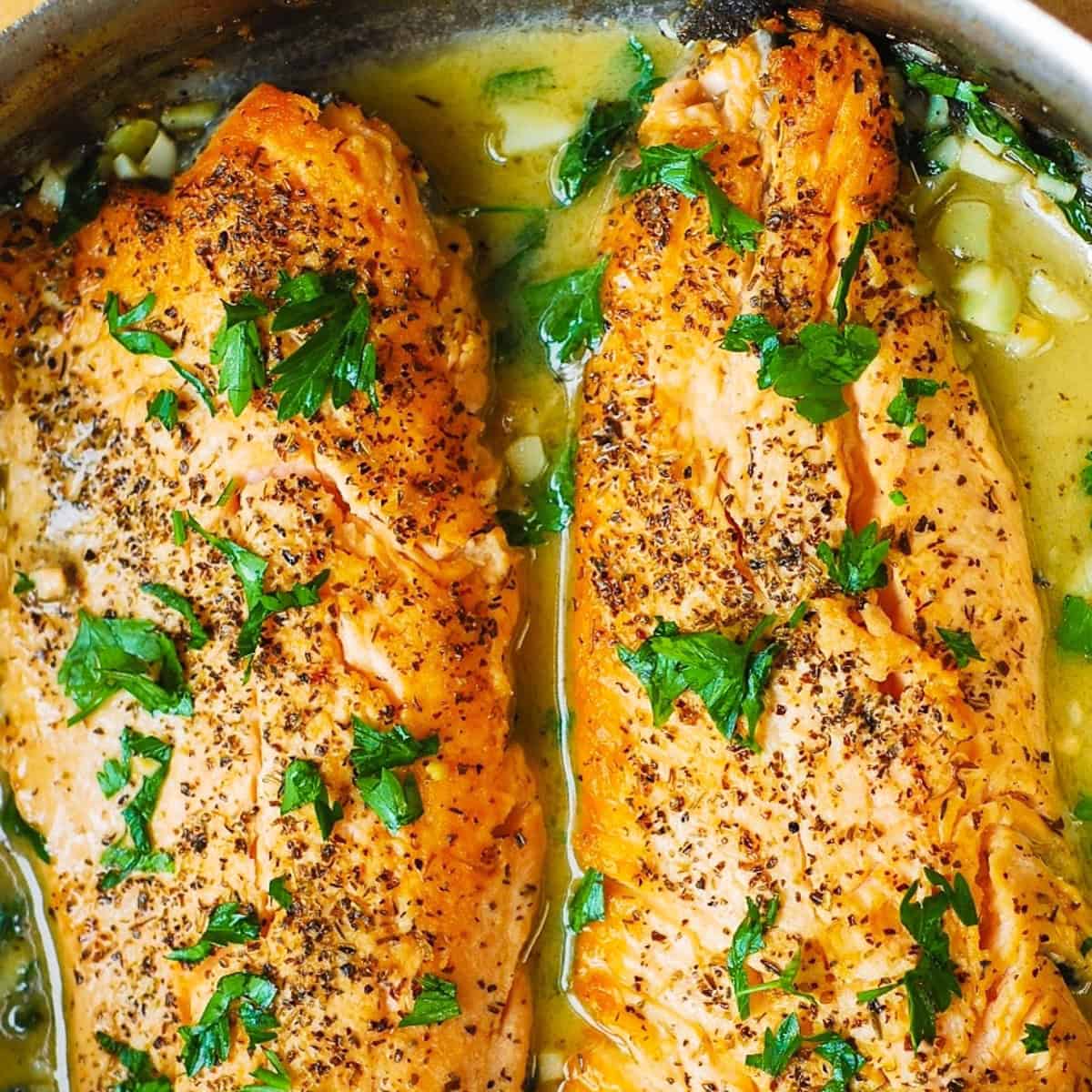 2 trout fillets in a garlic butter lemon sauce in a stainless steel pan.