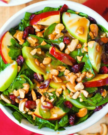 Apple Cranberry Spinach Salad with Cashews and Balsamic Vinaigrette - in a white bowl.