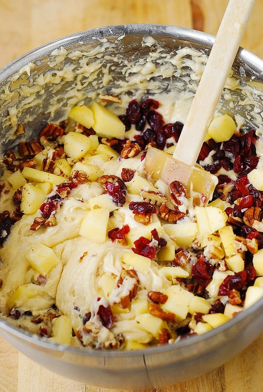 Mixing apples, pecans, cranberries into the cake batter in a mixing bowl