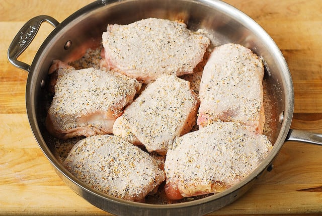 raw chicken thighs seasoned with lemon pepper seasoning in a stainless steel pan