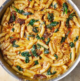 asiago chicken pasta with spinach and sun-dried tomatoes in a stainless steel pan