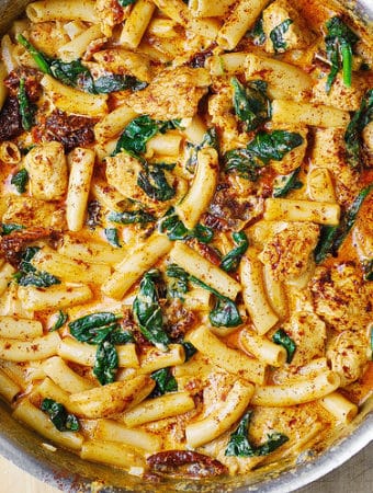 asiago chicken pasta with spinach and sun-dried tomatoes in a stainless steel pan