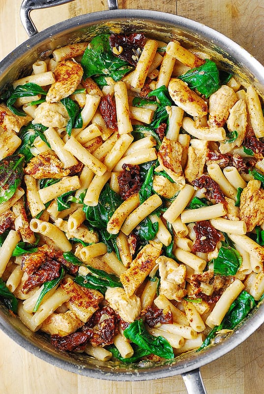 Creamy Asiago cheese pasta with chicken, sun-dried tomatoes, and spinach in a stainless steel skillet
