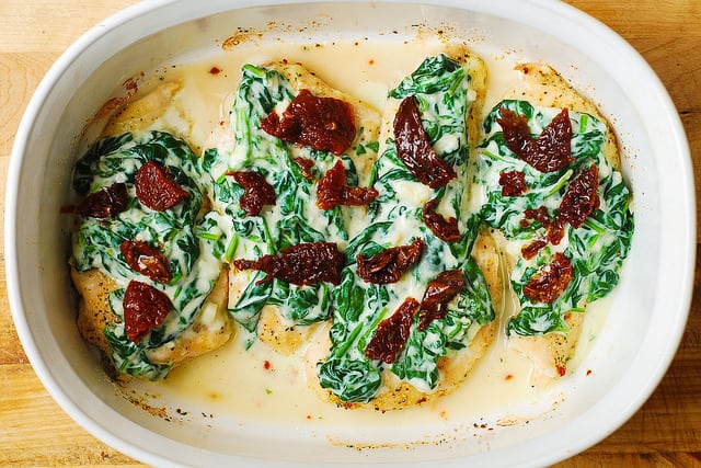 chicken breasts topped with creamed spinach and sun-dried tomatoes in a casserole dish