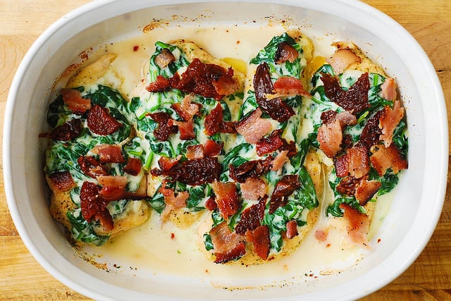 chicken breasts topped with creamed spinach, bacon, and sun-dried tomatoes in a casserole dish