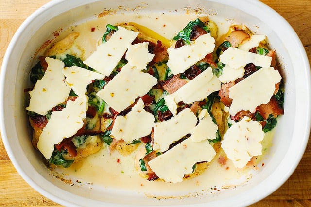 chicken breasts topped with creamed spinach, bacon, sun-dried tomatoes, and cheese in a casserole dish