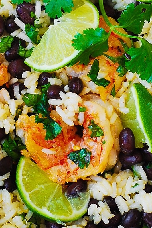 Black bean and cilantro-lime shrimp with rice with sliced limes and sprigs of cilantro