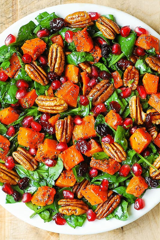 Butternut Squash and Spinach Salad with Pecans, Cranberries, Pomegranate Seeds and Poppy Seed Honey-Lime Dressing on a white plate