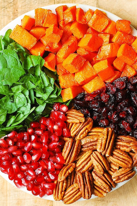 ingredients for Butternut Squash and Spinach Salad with Pecans, Cranberries, Pomegranate Seeds on a white plate
