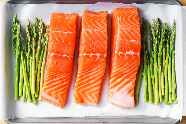 raw asparagus and raw salmon on parchment paper lined baking sheet