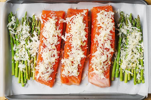 shredded Parmesan cheese and minced garlic sprinkled on top of raw salmon and raw asparagus on parchment paper lined baking sheet