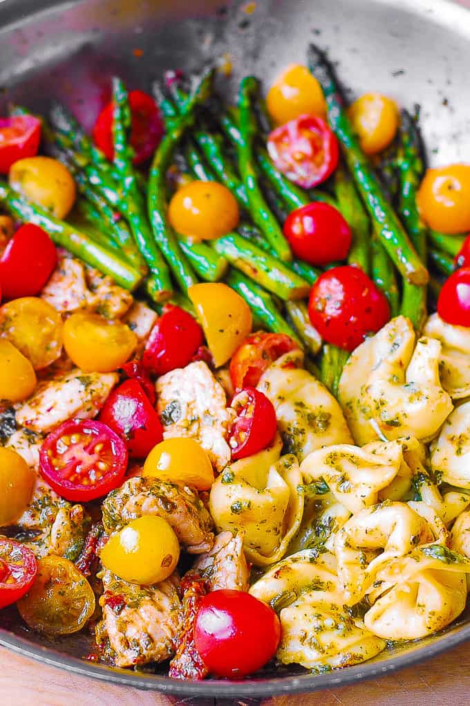 pesto chicken tortellini with cherry tomatoes and asparagus in a stainless steel skillet