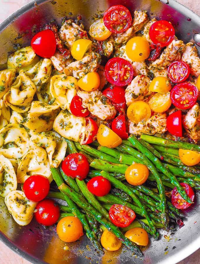 pesto chicken tortellini with cherry tomatoes and asparagus in a stainless steel skillet