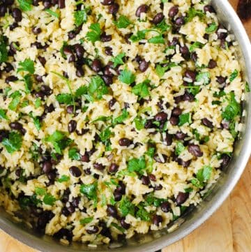 A close-up of a stainless steel pan filled with yellow rice, black beans, and fresh cilantro leaves, creating a colorful and vibrant dish.