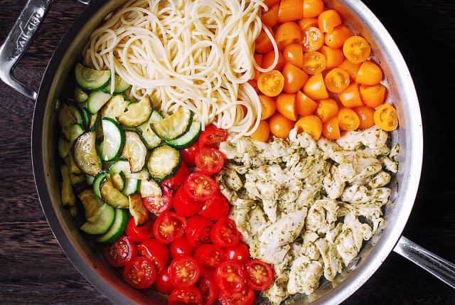 cooked sliced zucchini, sliced red cherry tomatoes, basil pesto chicken, sliced orange cherry tomatoes, cooked spaghetti - arranged in a stainless steel skillet
