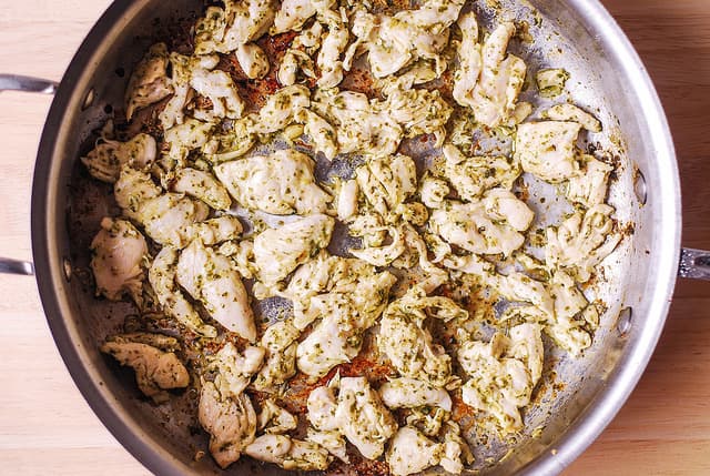 Cooking sliced chicken with basil pesto in a stainless steel skillet