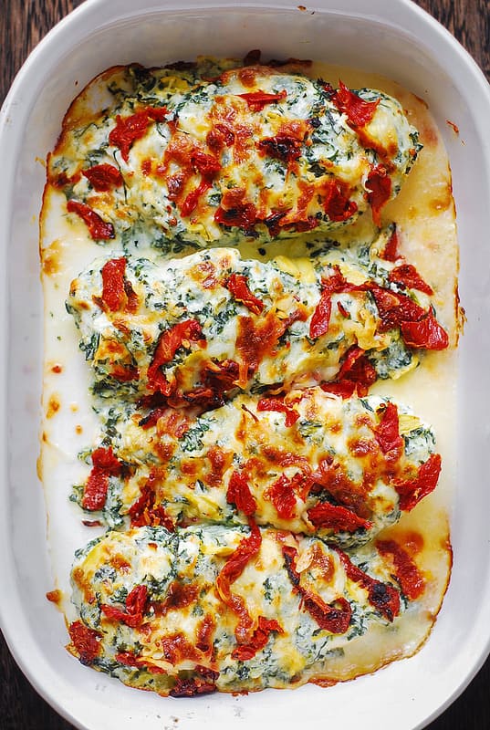 Chicken Florentine Bake - chicken breasts stuffed on top with homemade spinach-artichoke dip, sun-dried tomatoes, Mozzarella cheese - in a white casserole dish.