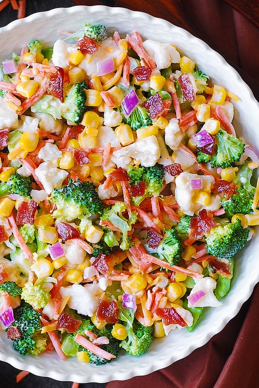 Creamy Broccoli, Cauliflower, Corn, Bacon Salad with Sliced Carrots, Diced Red Onions, and shredded Sharp Cheddar Cheese in a salad bowl