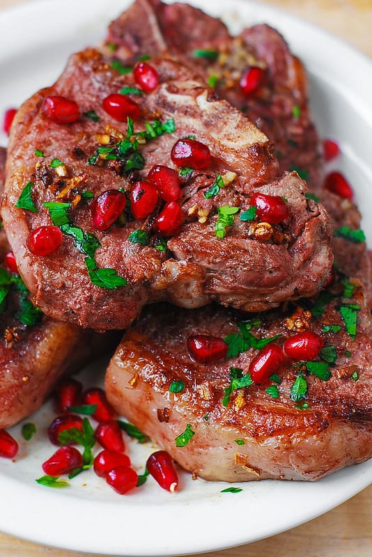 lamb chops with garlic and pomegranate seeds on a white plate