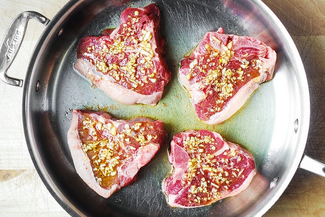 4 raw lamb chops with olive oil and garlic in a stainless steel pan