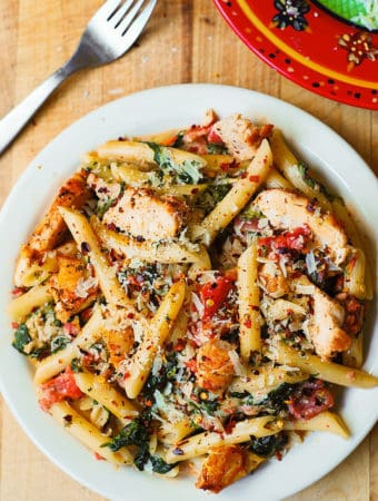 Chicken and Bacon Pasta with Spinach and Tomatoes in Garlic Cream Sauce on a white plate