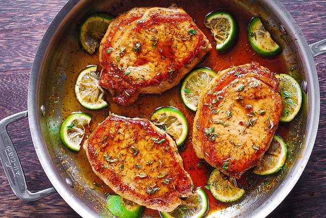 pork chops seasoned with salt and pepper, cooked in a stainless steel skillet with honey, lime, balsamic vinegar glaze and sprinkled with fresh thyme leaves