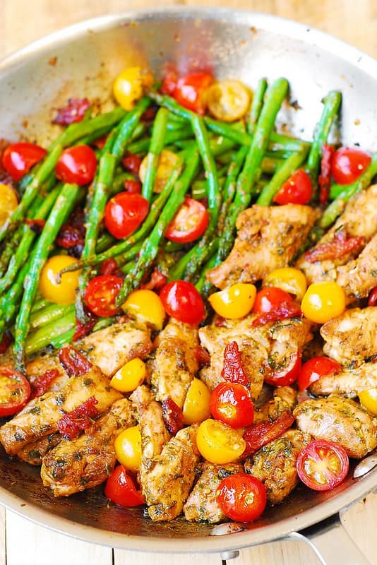 One-Pan Pesto Chicken and Veggies (asparagus and cherry tomatoes) in a stainless steel pan